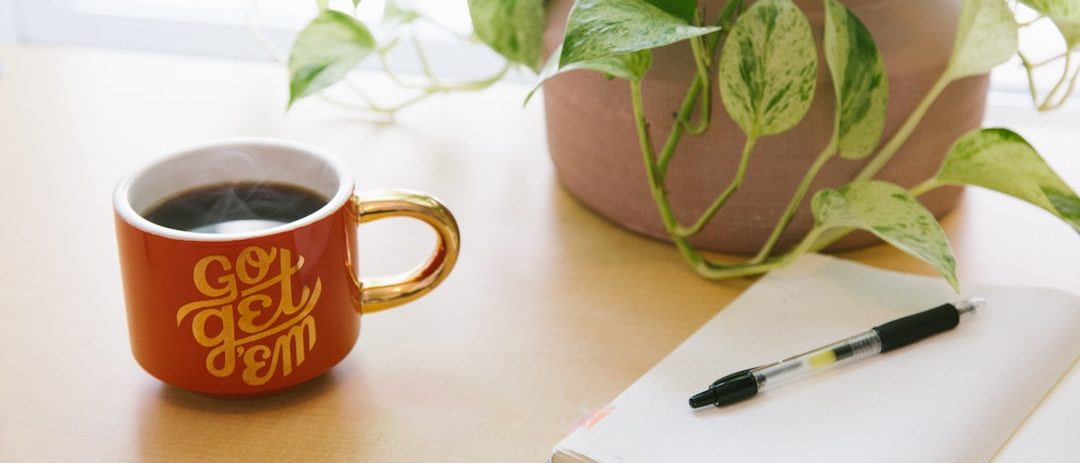 black retractable pen on opened book beside red and white go get'em-printed coffee cup