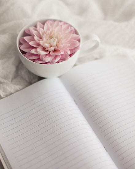 a white cup with a pink flower in it next to an open notebook