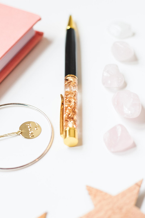 Gold filigree pen on table with journals, gold necklace and white rose petals