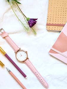 round gold-colored analog watch with pink leather band at 9:00