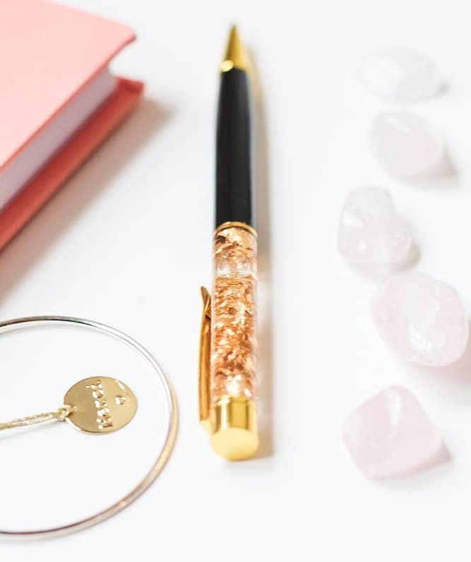 Gold filigree pen on table with journals, gold necklace and white rose petals