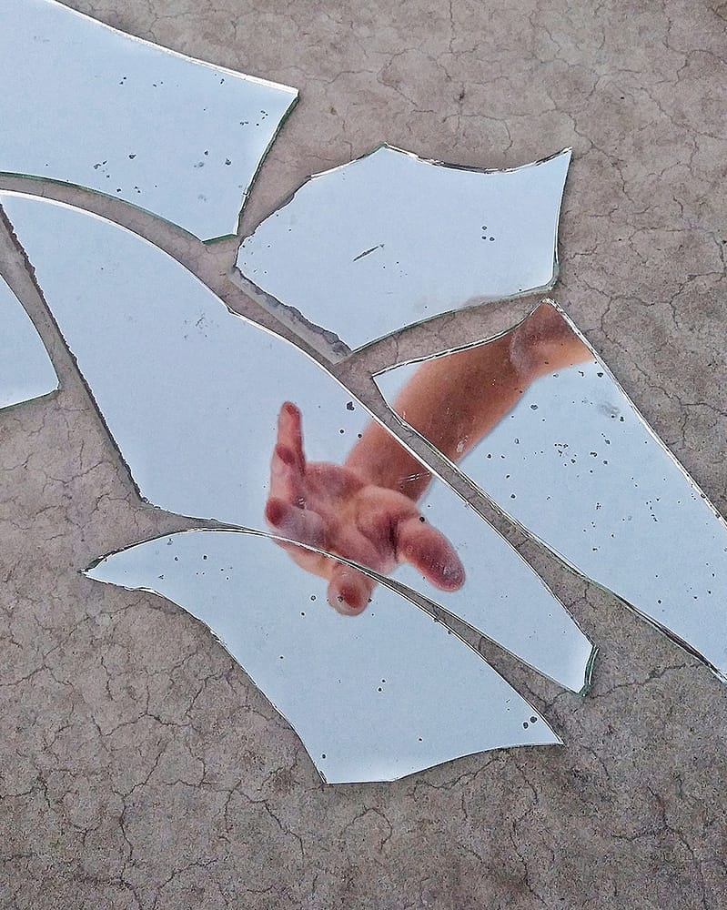 Mirror Fragments on Gray Surface With The Reflection Of A Person's Hand